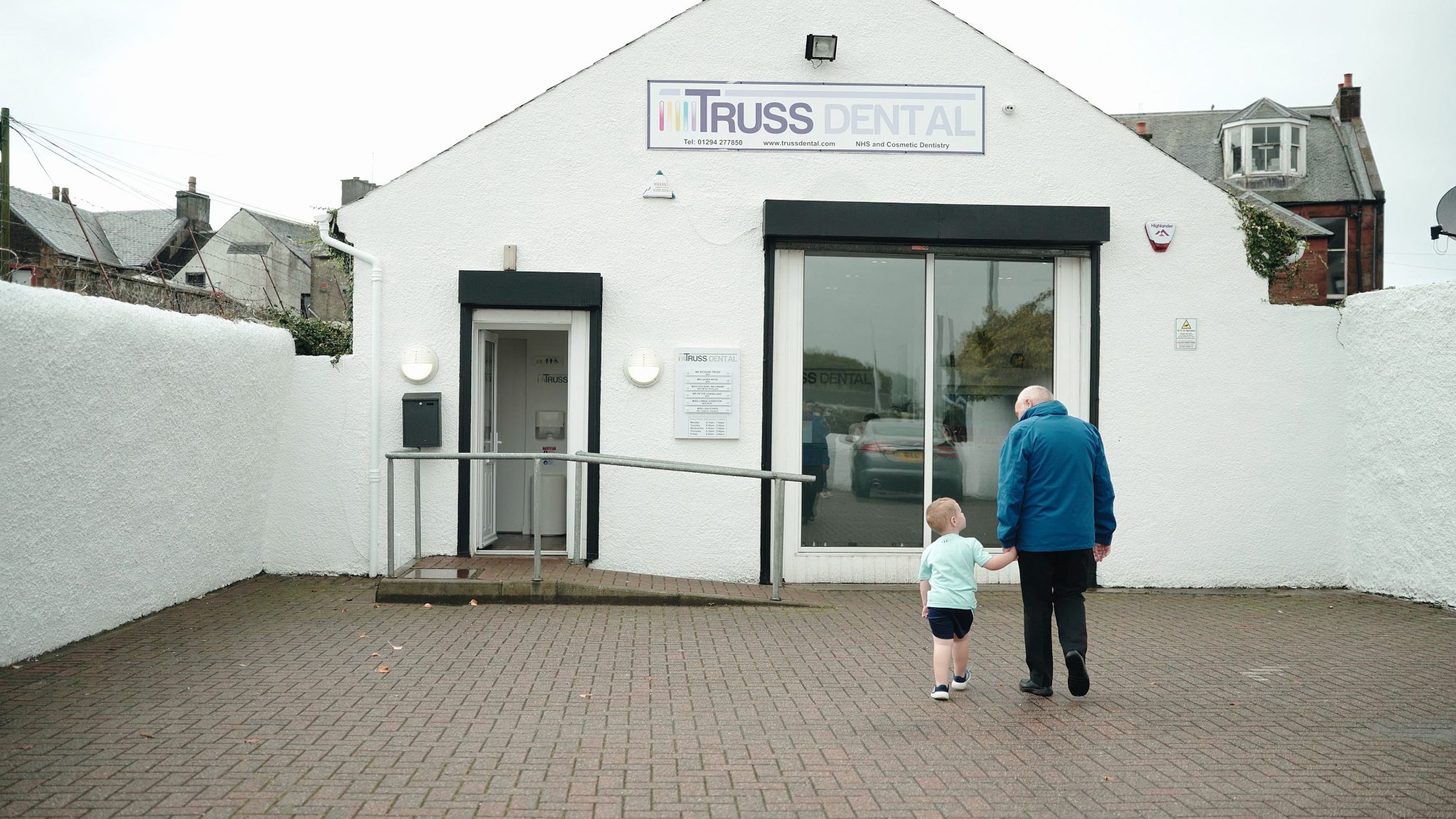 a man holding the hand of a kid both walking towards a dental practice, shoot for a promotional video